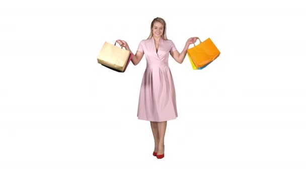 Junges blondes Mädchen im rosa Kleid, das vor der Kamera Einkaufstüten zeigt und auf weißem Hintergrund läuft. — Stockvideo