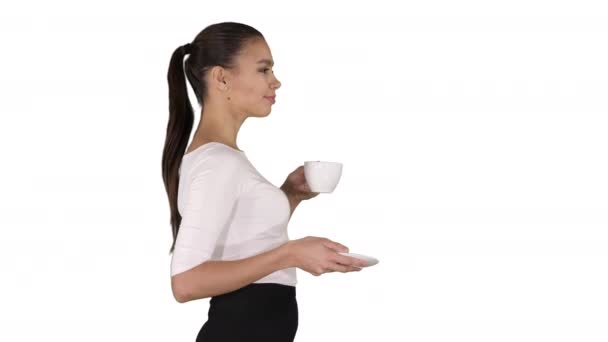 Bella donna bruna con tazza bianca con tè o caffè che cammina su sfondo bianco. — Video Stock