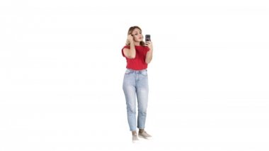 Güzel genç bir kadın maskara kullanıyor ve beyaz arka planda akıllı telefonuna bakıyor..
