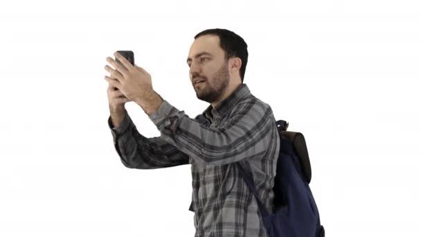Guapo joven llevando mochila y tomando una foto de sí mismo sobre fondo blanco . — Vídeo de stock