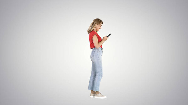 Casual young woman typing on mobile phone on gradient background.