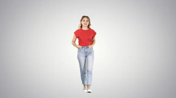 Mujer rubia caminando con las manos en los bolsillos y hablando con la cámara en un fondo degradado . —  Fotos de Stock