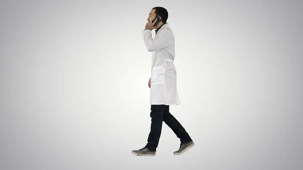 Médico joven hablando con móvil y walkind en el fondo gradiente . — Foto de Stock