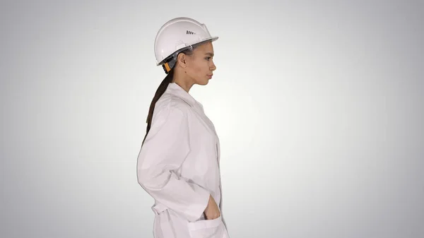 Mujer en bata blanca poniéndose un sombrero duro mientras camina sobre un fondo degradado . —  Fotos de Stock