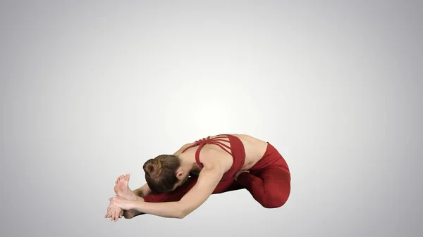 Jovem mulher atraente praticando ioga, sentado na cabeça para o joelho para frente Bend exercício, Janu Sirsasana pose no fundo gradiente . — Fotografia de Stock