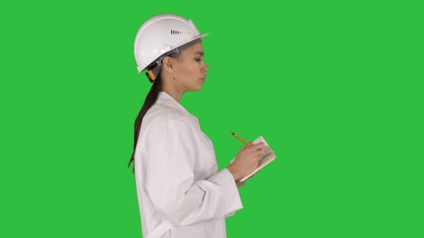 Woman engineer with helmet is holding pen and checklist putting something down while walking on a Green Screen, Chroma Key. — 비디오