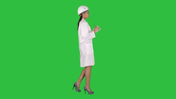 Donna ingegnere con casco sta tenendo penna e lista di controllo mettendo giù qualcosa mentre si cammina su uno schermo verde, Chroma Key . — Video Stock