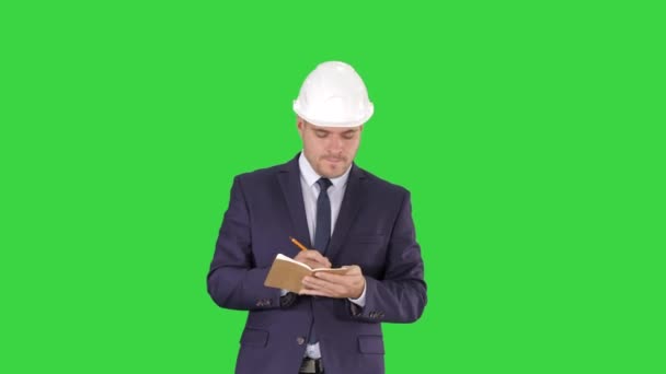 Engenheiro de terno e capacete andando e escrevendo notas no bloco de notas em uma tela verde, Chroma Key . — Vídeo de Stock