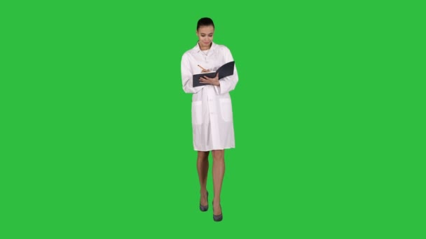 Espressivo giovane medico femminile con idea creativa che tiene il taccuino e cammina su uno schermo verde, chiave cromatica . — Video Stock