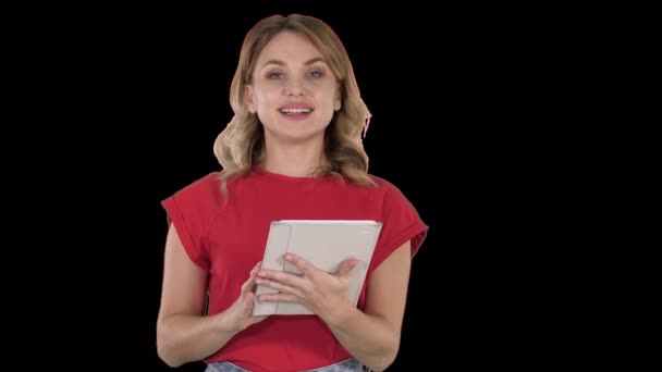 Mujer presentadora en camiseta roja sosteniendo una tableta pasando páginas y hablando con la cámara, Alpha Channel — Vídeo de stock
