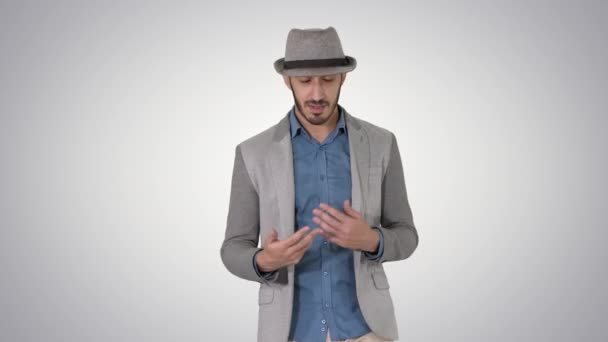 Hombre alegre positivo con estilo de moda que usa camisa casual y sombrero de sol caminando y hablando con la cámara en el fondo de gradiente . — Vídeos de Stock