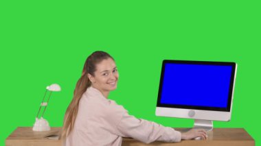 Ofiste bir bilgisayar ile masada oturan neşeli kadın ve yeşil ekranda Mavi Ekran Mock-up Ekran gülümseyen kamera bakarak, Chroma Anahtar.