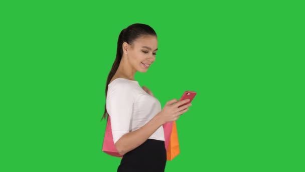 Mulher bonita usando um telefone móvel andando e segurando sacos de compras em uma tela verde, Chroma Key . — Vídeo de Stock