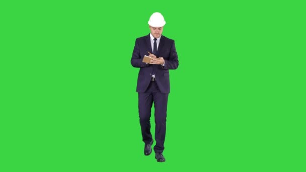 Инженер в костюме и шлеме ходит и пишет заметки в блокноте на зеленом экране, Chroma Key . — стоковое видео