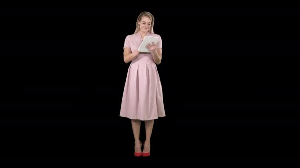 Όμορφη νεαρή γυναίκα σε ροζ φόρεμα κρατώντας δισκίο και κοιτάζοντας σε αυτό, κανάλι άλφα — Αρχείο Βίντεο