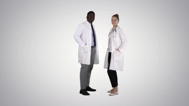 Dwóch białych i afro amerykańskich uśmiechniętych lekarzy patrzących w kamerę na gradientowym tle. — Wideo stockowe