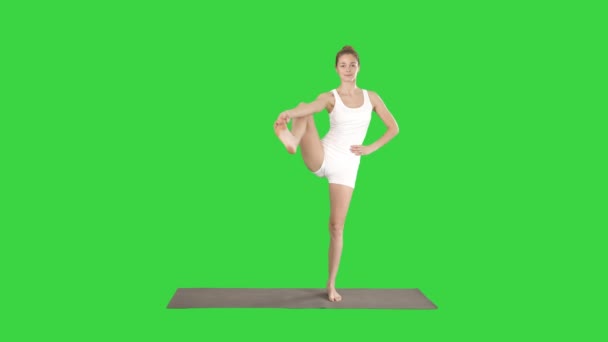 Krásná usměvavá mladá žena dělá jóga cvičení na rohoži, stojící v pozici Vrksasana, pozice stromu na zelené obrazovce, chroma klíč. — Stock video