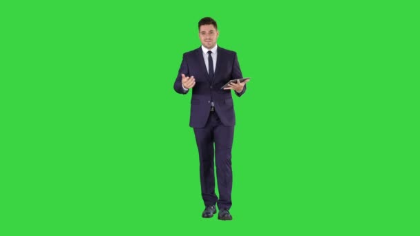 Uomo d'affari strisciare pagine su un tablet e parlare con la fotocamera spiegando qualcosa mentre si cammina su uno schermo verde, Chroma Key . — Video Stock