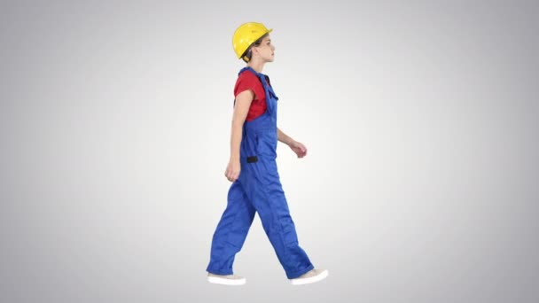 Mujer joven trabajadora de la construcción en hardhat amarillo caminando sobre fondo degradado. — Vídeo de stock