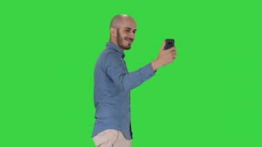 Yeşil Ekranda yürürken selfie çeken mutlu gülümseyen yakışıklı genç adam, Chroma Key.