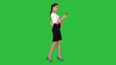 Alışveriş çantalarıyla yürüyen genç bir kadın yeşil ekranda cep telefonuyla konuşuyor, Chroma Key..