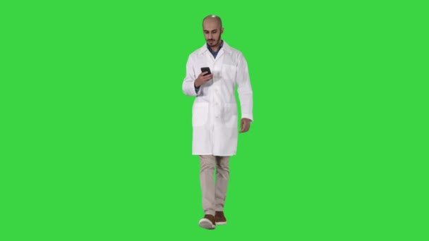 Male arab doctor texting message on the phone while walking on a Green Screen, Chroma Key. — Stock Video