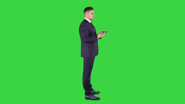 デジタルタブレットに触れ、グリーンスクリーンで彼の前のオブジェクトをチェックする若いビジネスマン、クロマ・キー. — ストック動画