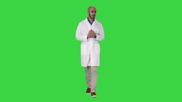 医療ユニフォームを着た中年の医者の男性は、グリーンスクリーン上のカメラを見て手のひらを指し示し、クロマキー. — ストック動画