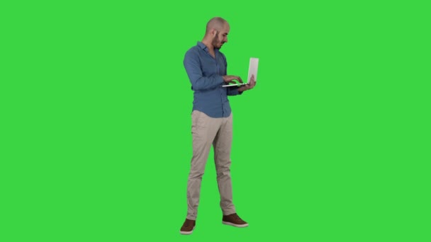 Молодой бизнесмен с Ближнего Востока, стоящий и печатающий на ноутбуке, держа его в руках на зеленом экране, Chroma Key . — стоковое видео