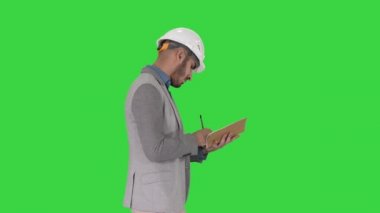 Rahat giysiler ve sert şapka lı Arap adam Yeşil Ekran, Chroma Key üzerinde kontrol listesi aşağı yazma.