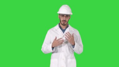 Beyaz cüppe ve kask bilim adamı el ile yan gösteren ve Yeşil Ekranda kameraya açıklayan, Chroma Anahtar.