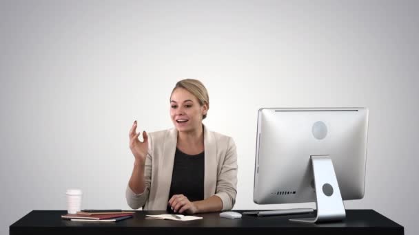 Захоплена бізнес-леді розмовляє на камеру, сидячи за столом на градієнтному фоні . — стокове відео