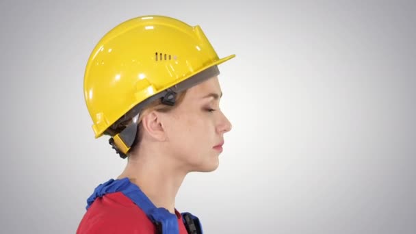 A jovem engenheira com capacete de segurança amarelo andando e sorrindo no fundo gradiente . — Vídeo de Stock