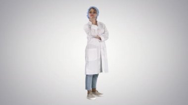Sırıtkan, kendine güvenen genç bir kadın doktor kollarını kavuşturup arka planda duruyor..
