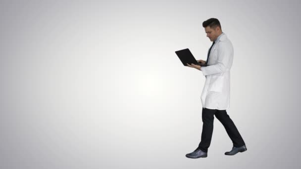 Médico alegre com laptop rindo depois de dar um olhar sério para a câmera no fundo gradiente . — Vídeo de Stock