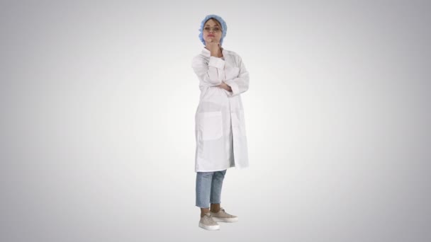 Sorridente fiducioso giovane donna medico in piedi con le braccia incrociate su sfondo sfumato. — Video Stock