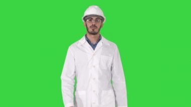 Young engineer in robe and helmet putting glasses on while walking on a Green Screen, Chroma Key.