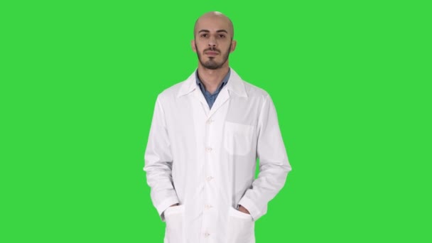 Arabischer gutaussehender Arzt, der seine Uniform trägt und die Hände in den Taschen auf einem grünen Bildschirm trägt, Chroma-Schlüssel. — Stockvideo