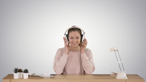 Jovem mulher sorrindo colocando fones de ouvido e ouvindo música no fundo gradiente. — Vídeo de Stock