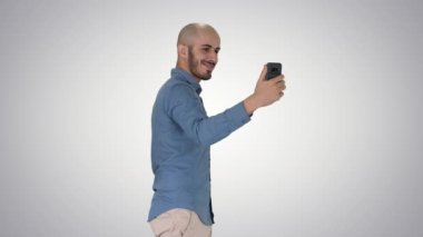 Degrade arka planda yürürken mutlu gülümseyen yakışıklı genç adam selfie yapma.