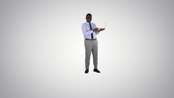 Разговаривая с камерой молодой африканский мужчина с ноутбуком в руках на градиентном фоне. — стоковое видео