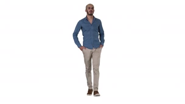 Handsome young arabic man wearing a casual outfit walking, putting his both hands in his pockets on white background. — Stock Video