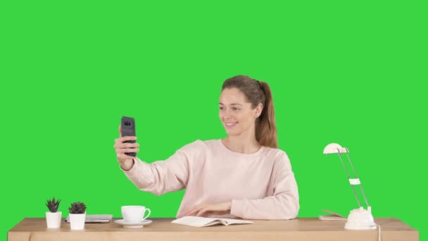 Schöne Frau macht ein Selfie mit ihrem Handy am Schreibtisch auf einem grünen Bildschirm, Chroma-Schlüssel. — Stockvideo
