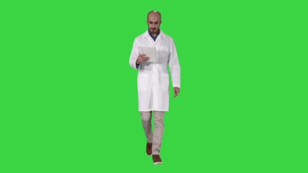 Mature male doctor holding digital tablet using it and walking on a Green Screen, Chroma Key. — Stock Video