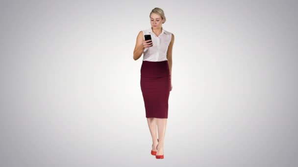 Mujer emocionada caminando y leyendo noticias increíbles en línea en un teléfono inteligente en el fondo del gradiente . — Vídeos de Stock