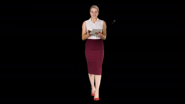 Glimlachende zakenvrouw met behulp van elektronische tabblad jatten en kijken naar de camera tijdens het wandelen, alfakanaal — Stockvideo