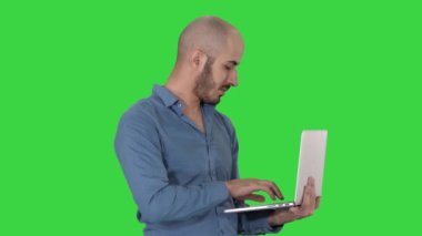 Genç Orta Doğu işadamı, ayakta ve dizüstü bilgisayar üzerinde bir yeşil ekran elinde tutarken yazarak, chroma key.