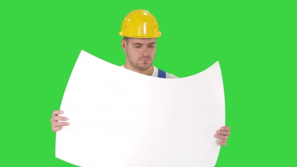 Nachdenklicher Bauarbeiter im Helm, der sich die Blaupause ansieht und auf einem grünen Bildschirm wandelt, Chroma-Schlüssel. — Stockvideo