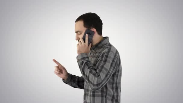 Portrait latéral d'un étudiant heureux marchant et parlant sur un téléphone portable sur fond de dégradé. — Video