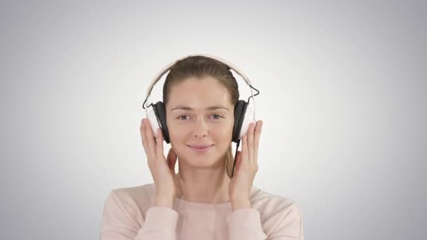 Eine junge Frau hört Musik über Kopfhörer auf dem Hintergrund des Gefälles. — Stockvideo